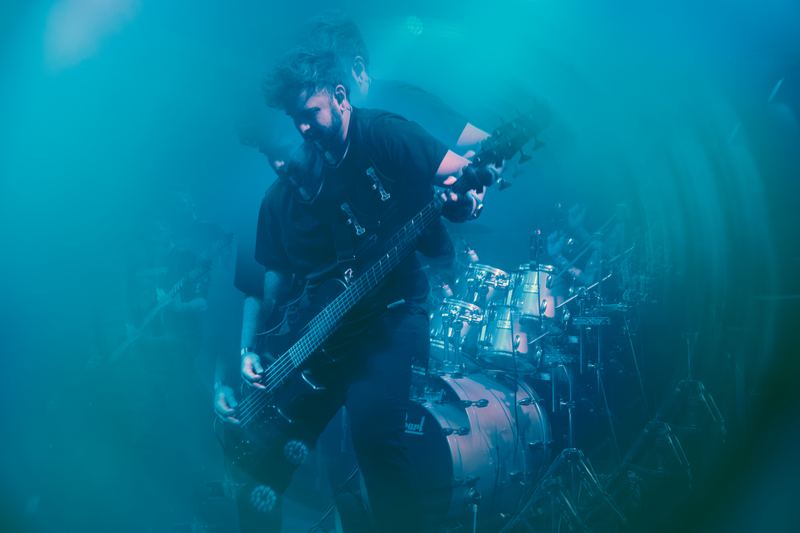 Bassist on stage in haze and cyan light, live concert