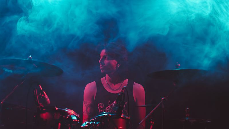 A drummer on stage in teal and magenta haze, live concert