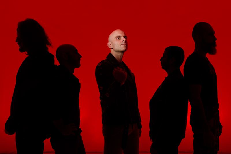 Group portrait: five musicians backlit against a red backdrop
