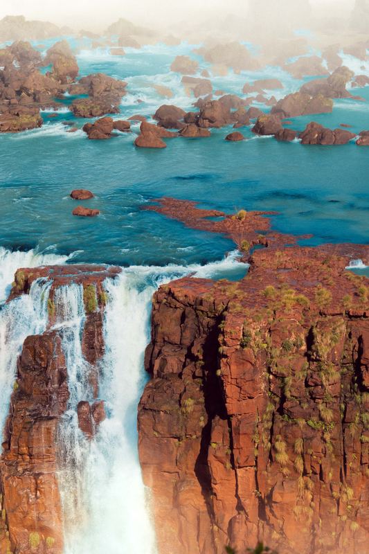 Waterfalls dropping from a red cliff into a turquoise river