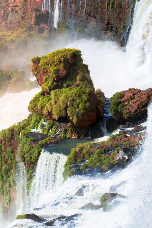 A moss-covered rock in the middle of the falls, white water all around