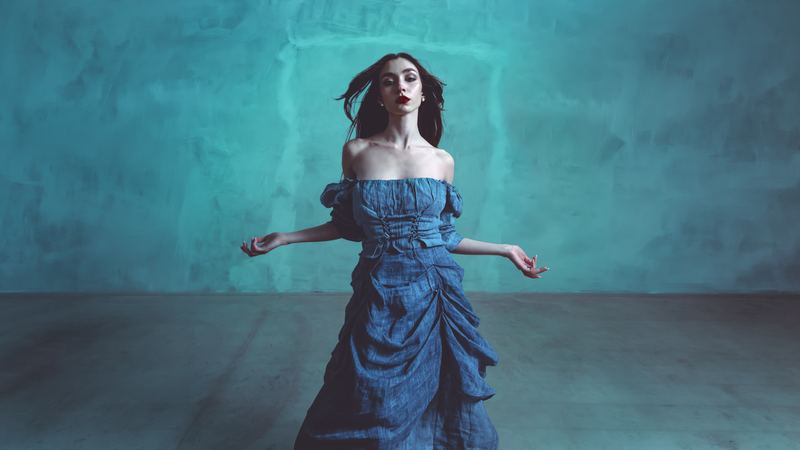 Ritratto di moda: abito di denim a balze, braccia aperte, fondale verde acqua