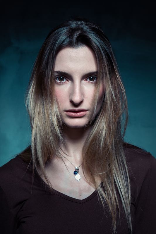 Primo piano di una donna con capelli lunghi e ciondolo, luce morbida su fondo scuro
