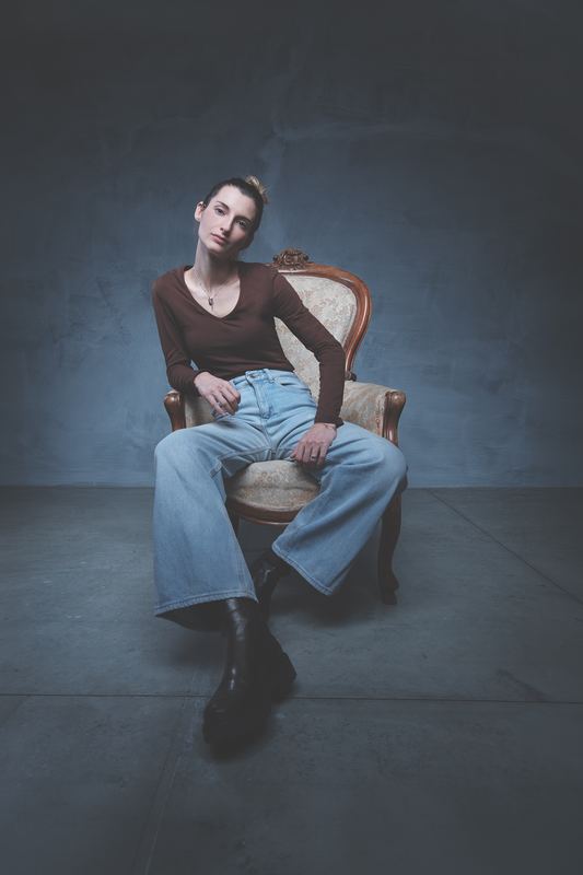 Ritratto di una donna seduta in poltrona antica, jeans a gamba larga, luce radente