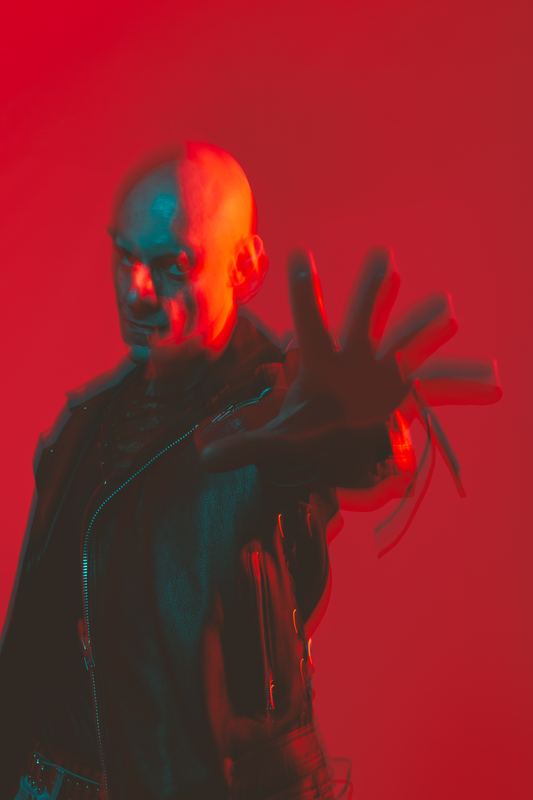 Ritratto su fondo rosso, uomo con la mano tesa verso la macchina fotografica