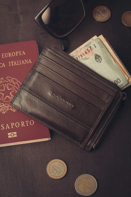 Portacarte in pelle con passaporto italiano, banconote e monete, still life da viaggio