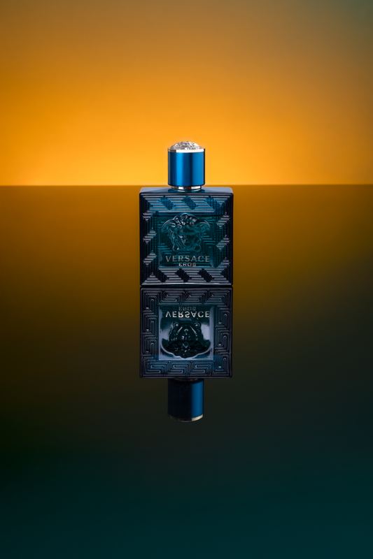 Boccetta di profumo scura riflessa su superficie lucida con luce arancio e verde