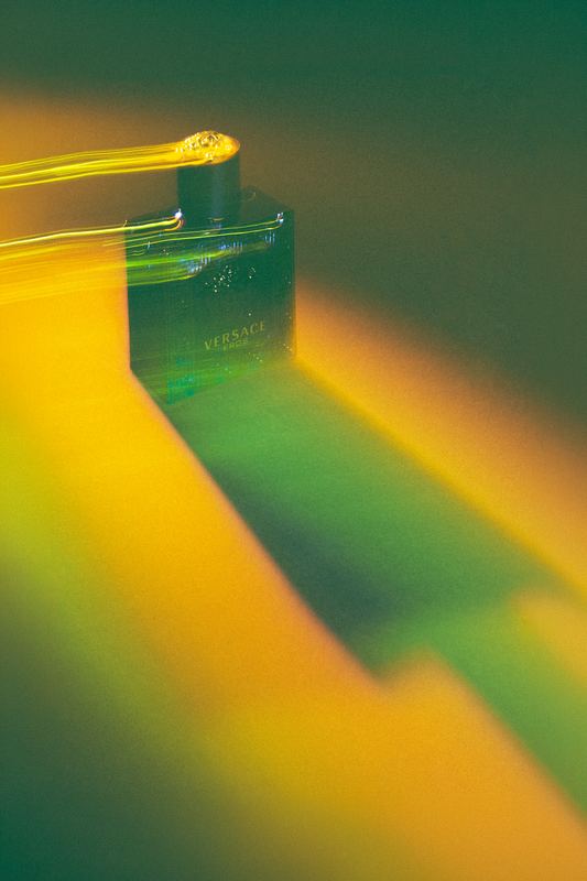 Boccetta di profumo attraversata da una scia di luce gialla e verde, still life creativo